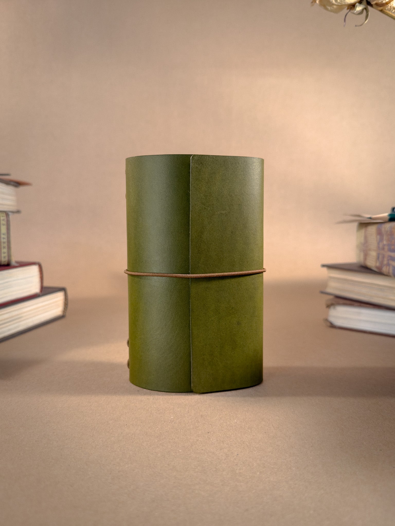 A pocket sized tri-fold green leather journal on a beige background